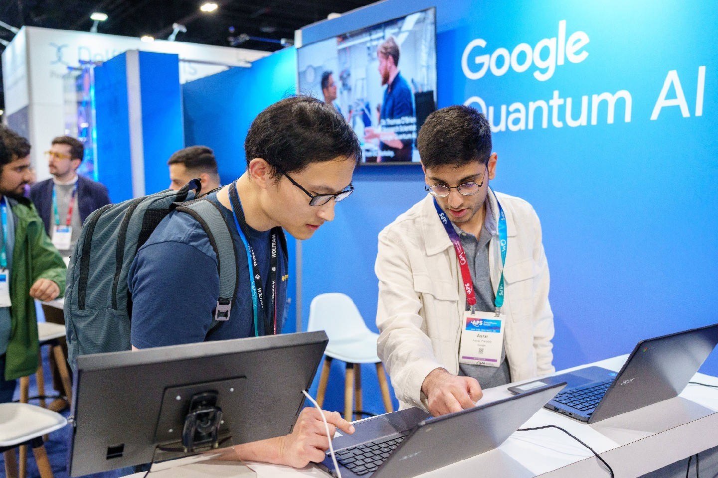 Two Global Physics Summit attendees look at a computer together in front of a large Google Quantum AI sign.