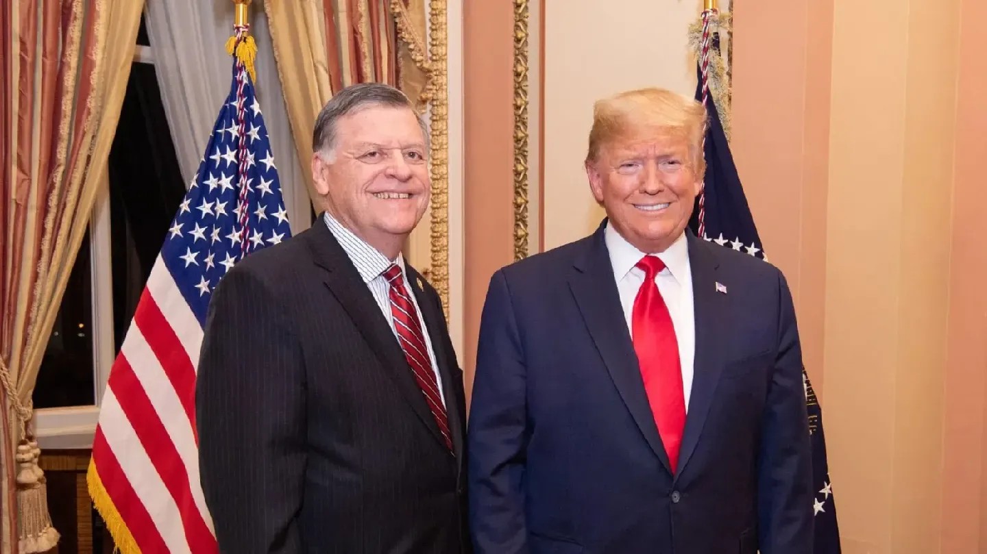 Rep. Cole and President Trump standing side by side, smiling, with flags in the background.
