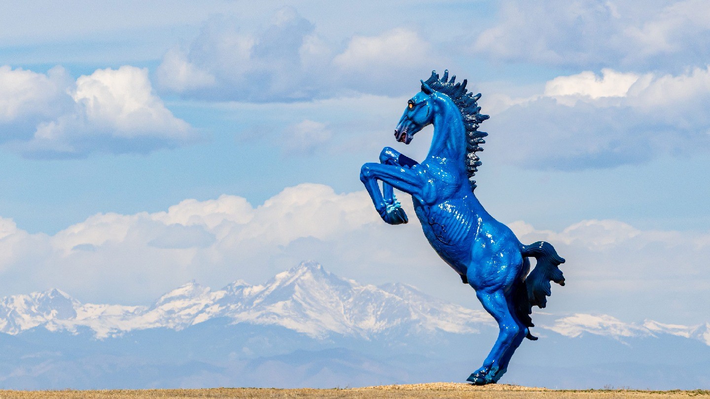 A blue stallion statue with glowing eyes, with the snow-covered Rocky Mountains visible in the background.