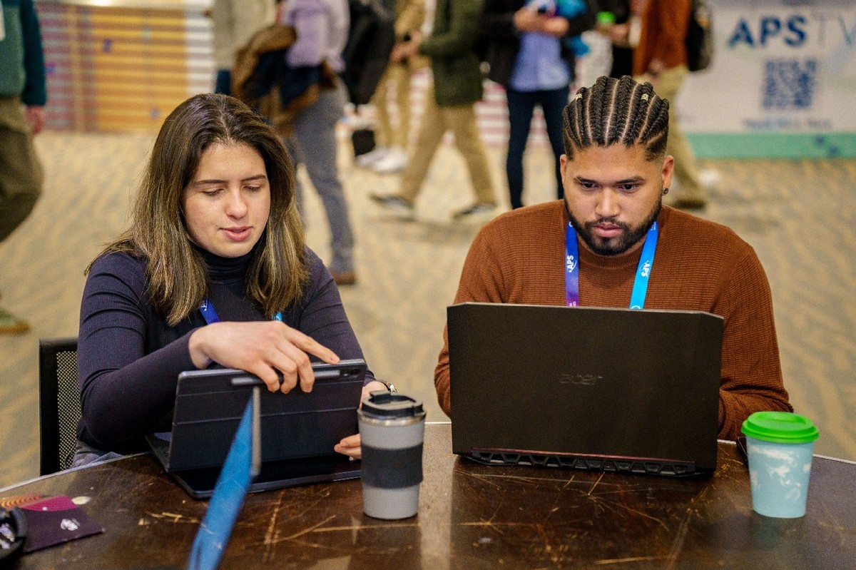 Two people sitting next to each other at a table, each using a laptop.