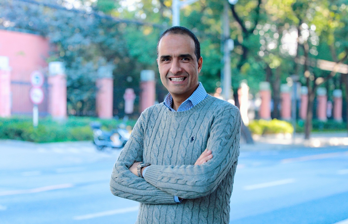 A photo of Badreddine Assouar, smiling with arms crossed, with sunlit trees behind him.