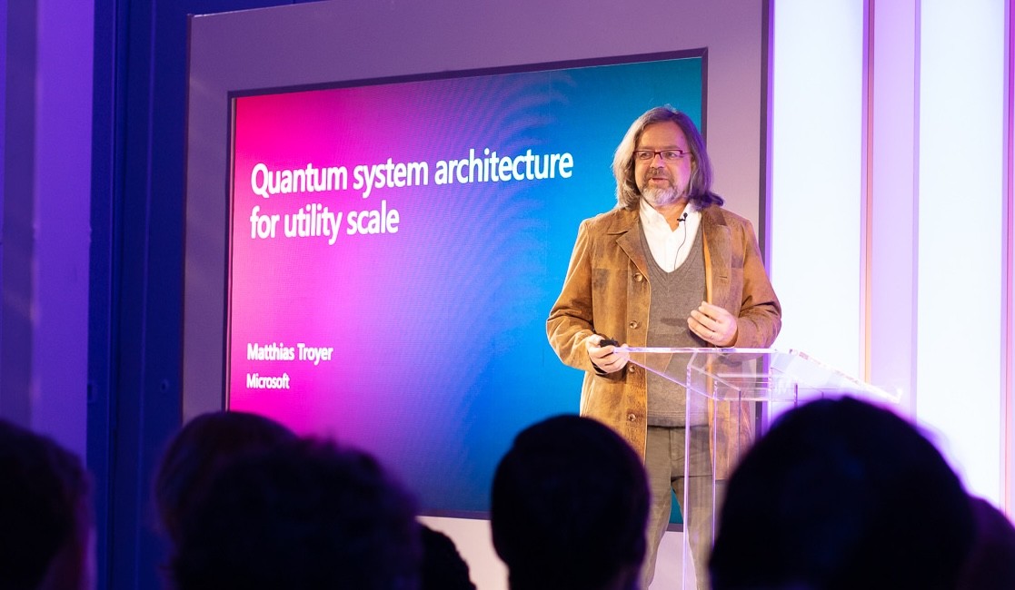 Matthias Troyer presents to the audience with a brightly colored Microsoft presentation visible behind him.