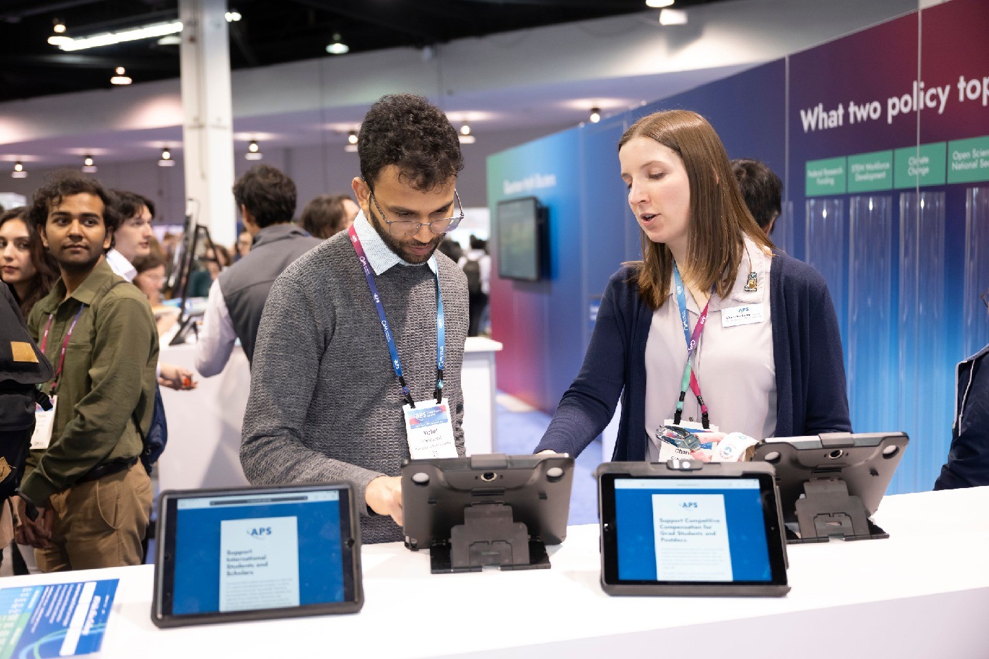An APS staff member (right) chats with a meeting attendee about submitting a letter to Congress, with other attendees visible in the background.