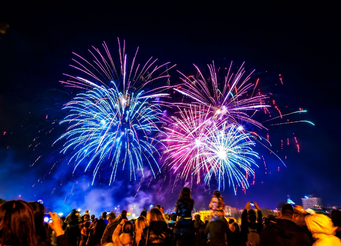 Several fireworks of different colors light up a dark sky above a crowd of people.
