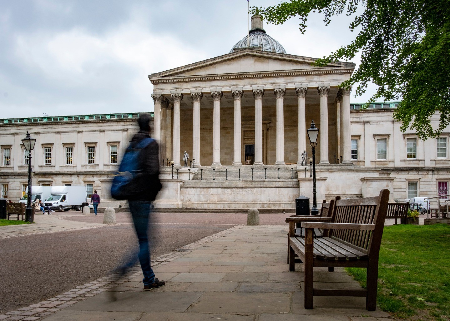 A blurred person walks in front of a college campus building.