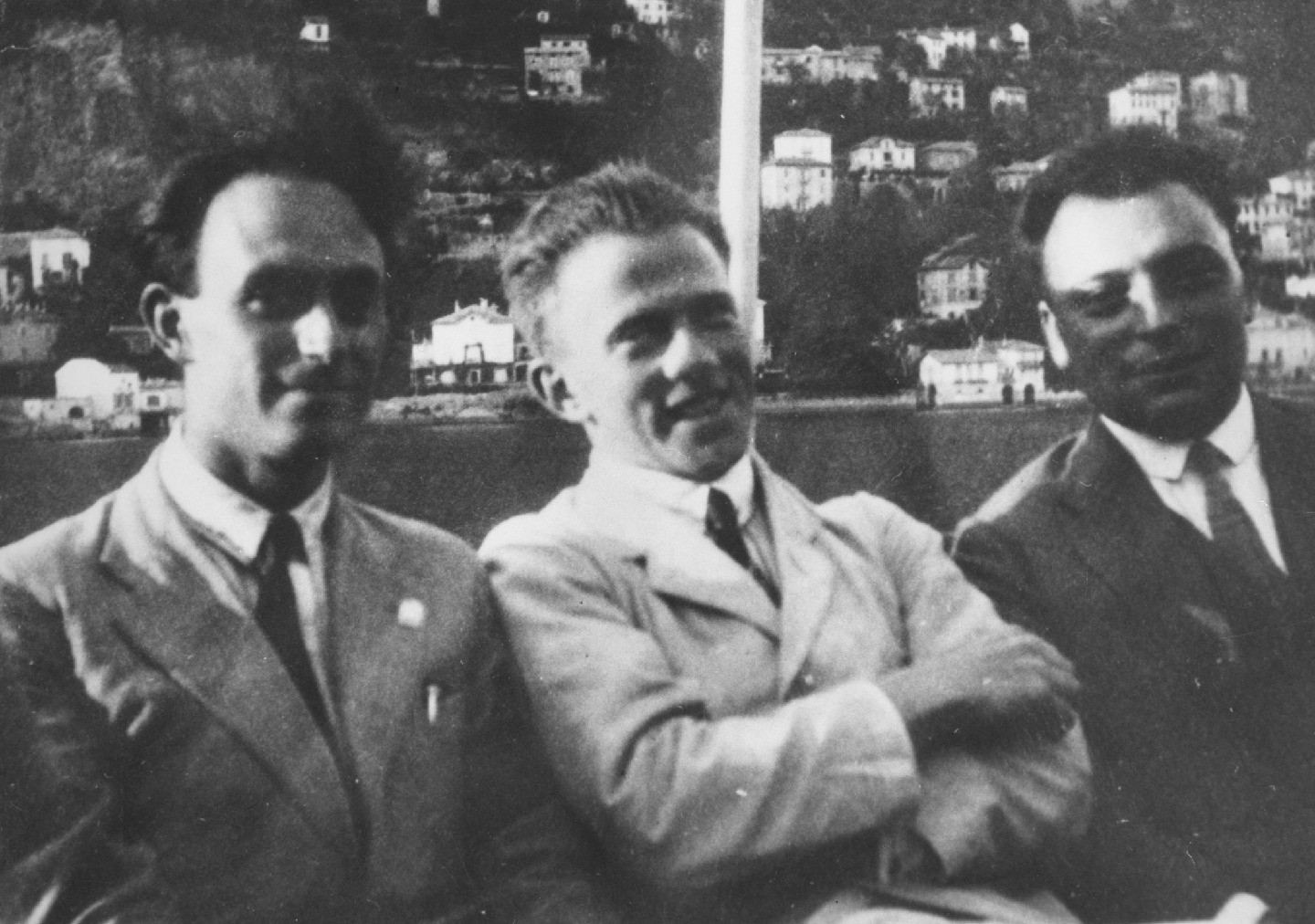 Black-and-white photo of three men in suits sitting next one another and smiling for the photo.