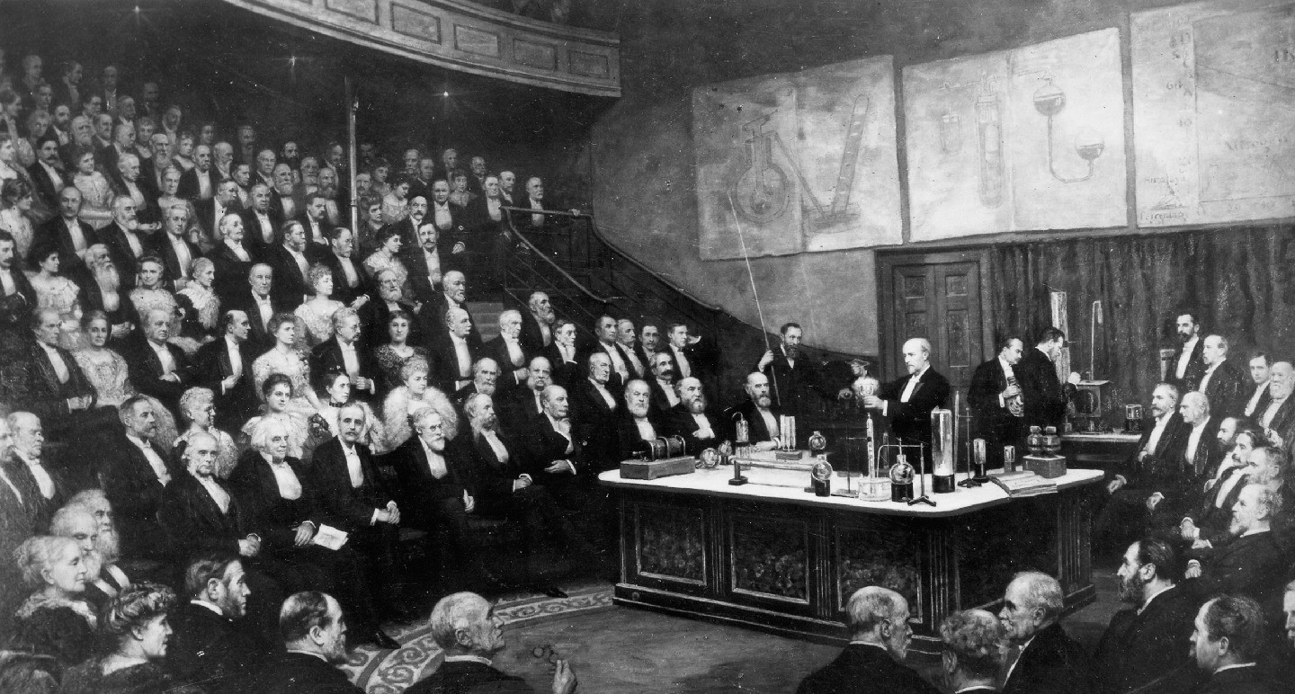 Black-and-white depiction of an audience in formal attire on tiered seating watching men below them behind a desk.