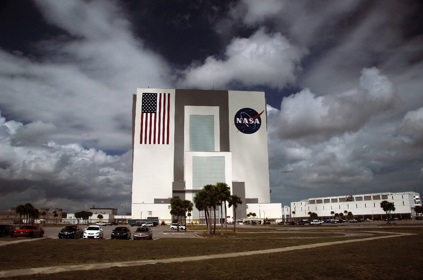 A large, blocky building with the NASA logo is visible under a gray, cloudy sky.