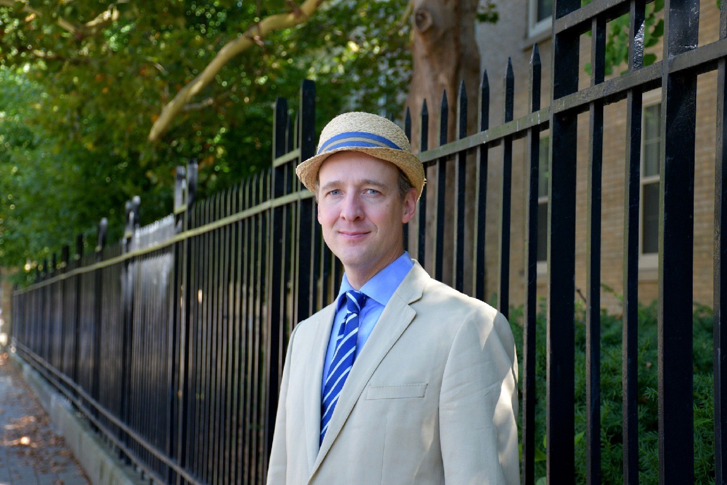 Anatole Lilienfeld stands outside a fence wearing a suit and hat.