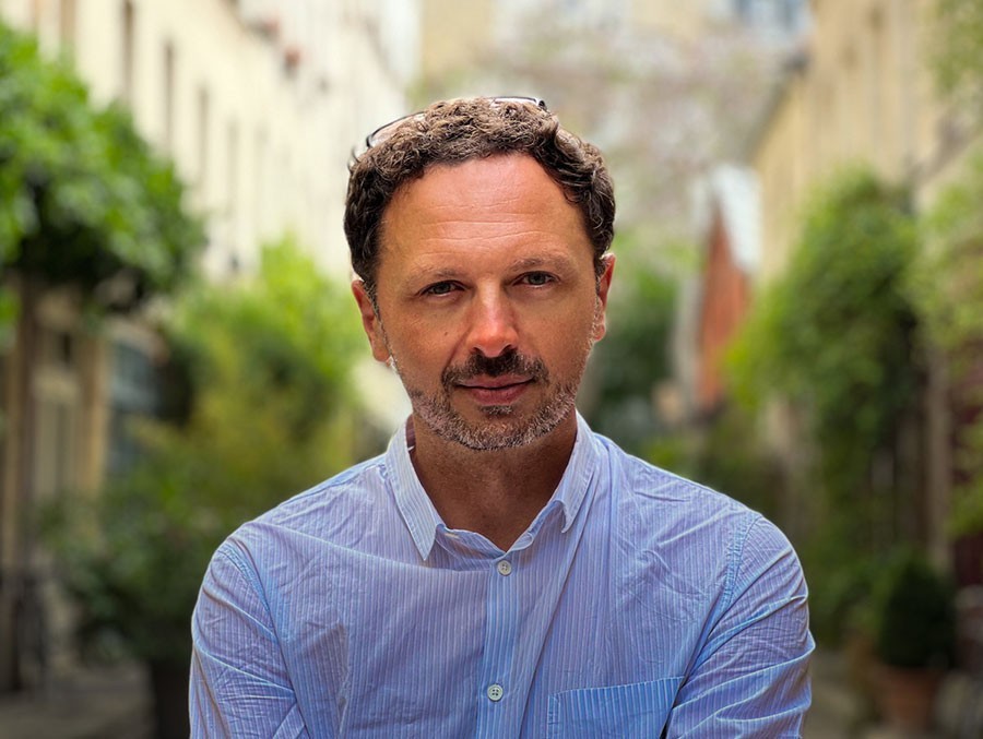 A headshot of Denise Bartolo, with greenery behind him.
