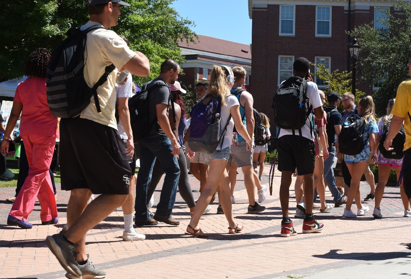 A crowd of college students, most with backpacks, walk on a bustling campus.