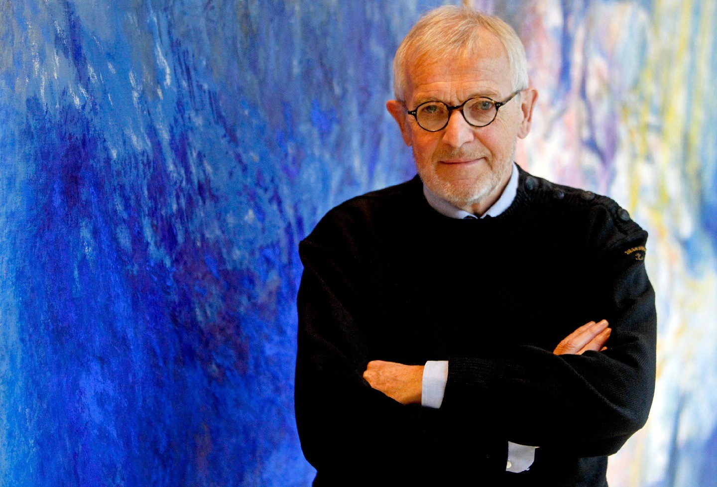 Francis Halzen, with arms crossed, stands next to a colorful blue wall.