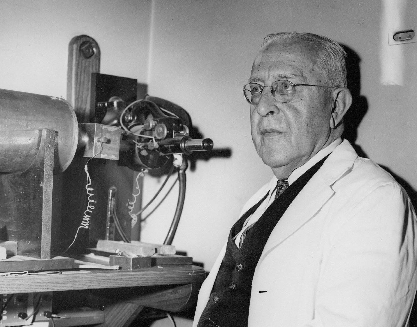 Black-and-white photo of Victory Hess standing near optical lab equipment.