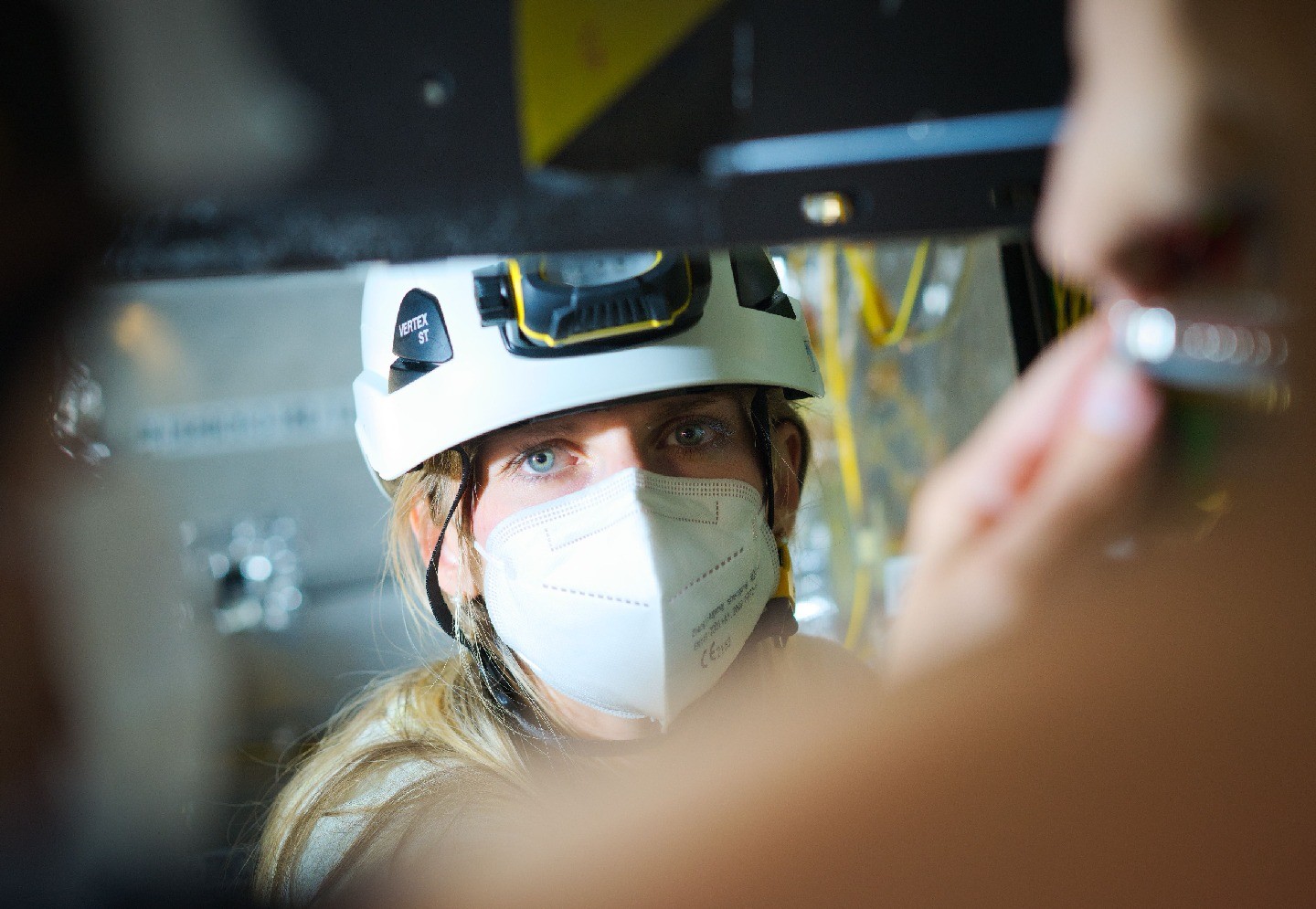 Karacheban, wearing a protective hard hat and a mask, peers past the camera.
