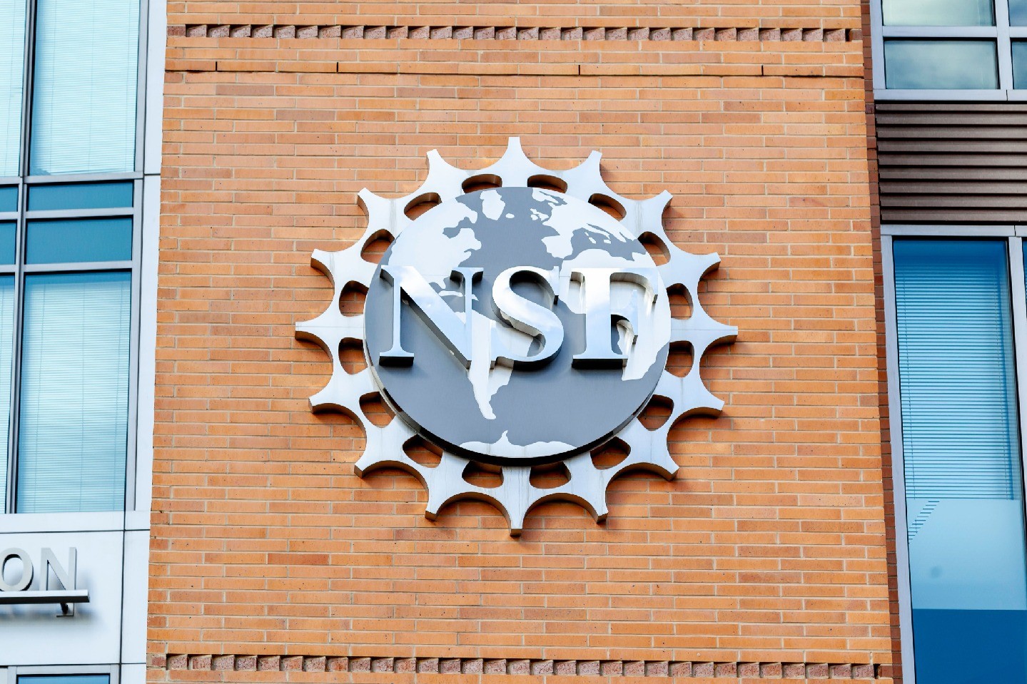 A silver, circular National Science Foundation seal, reading “NSF,” adorns a brick building facade.