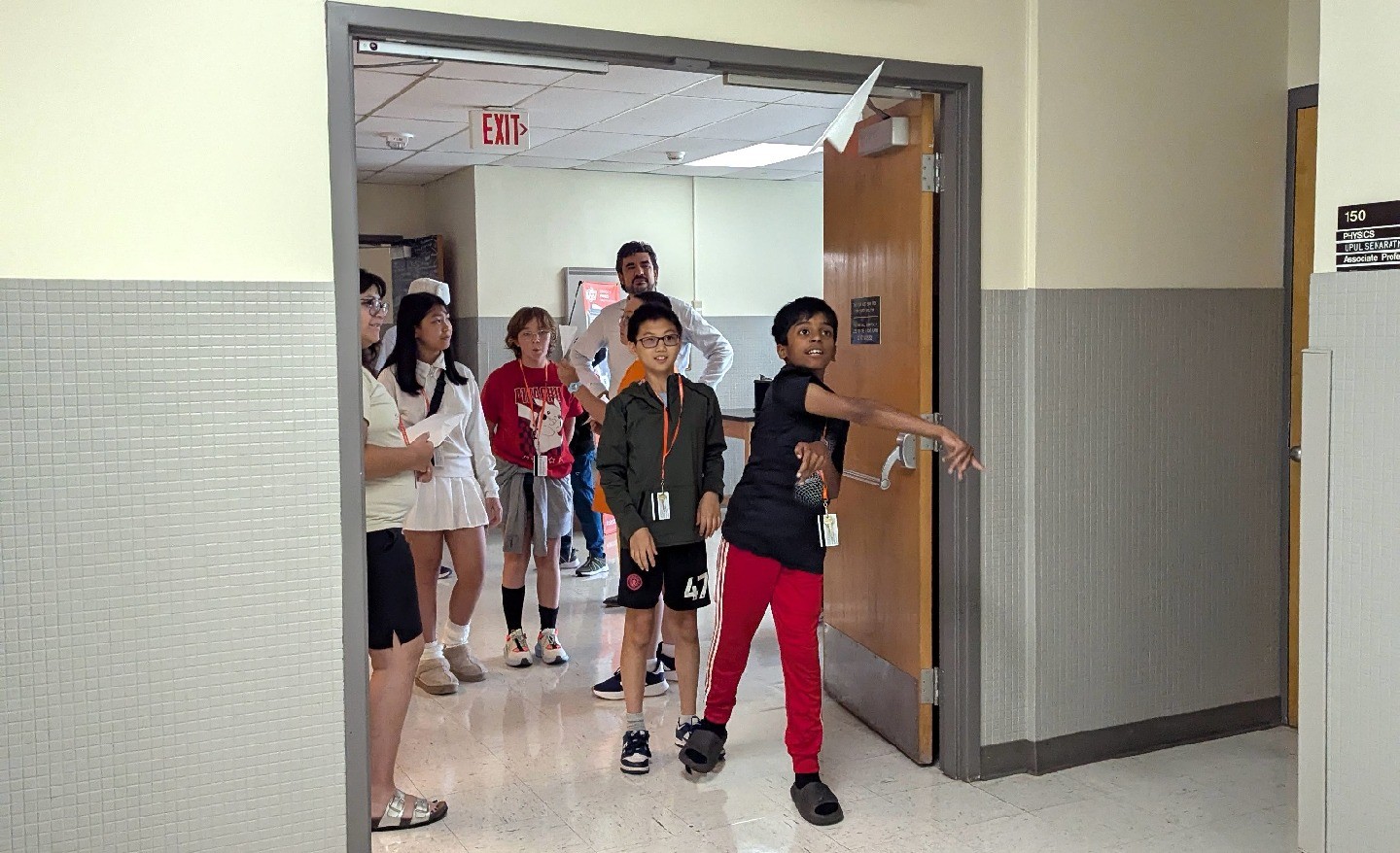 A camper throws a paper airplane in a doorway, with a group of other campers looking on.