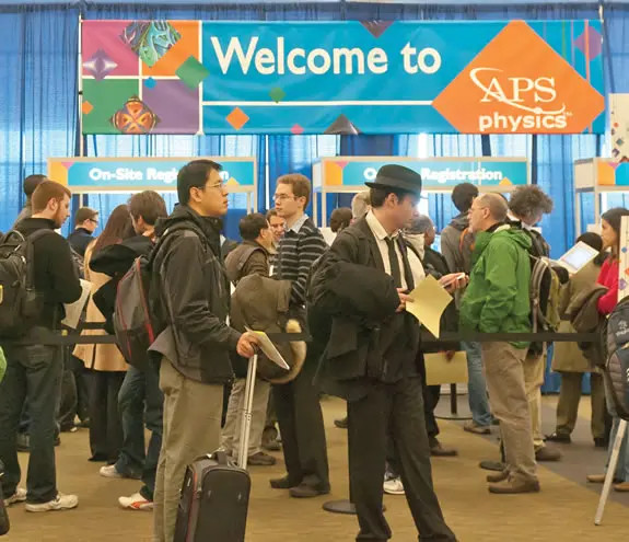 A crowd of people queuing in stanchions under a banner that reads: Welcome to APS Physics.