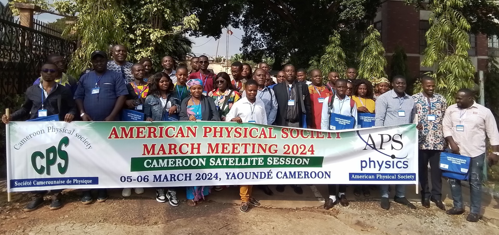 Dozens of people stand outdoors displaying a large APS event banner