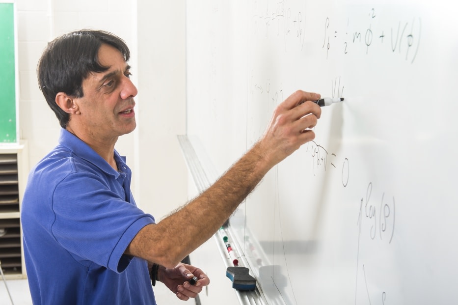 Bharat Ratra stands at a whiteboard writing equations.