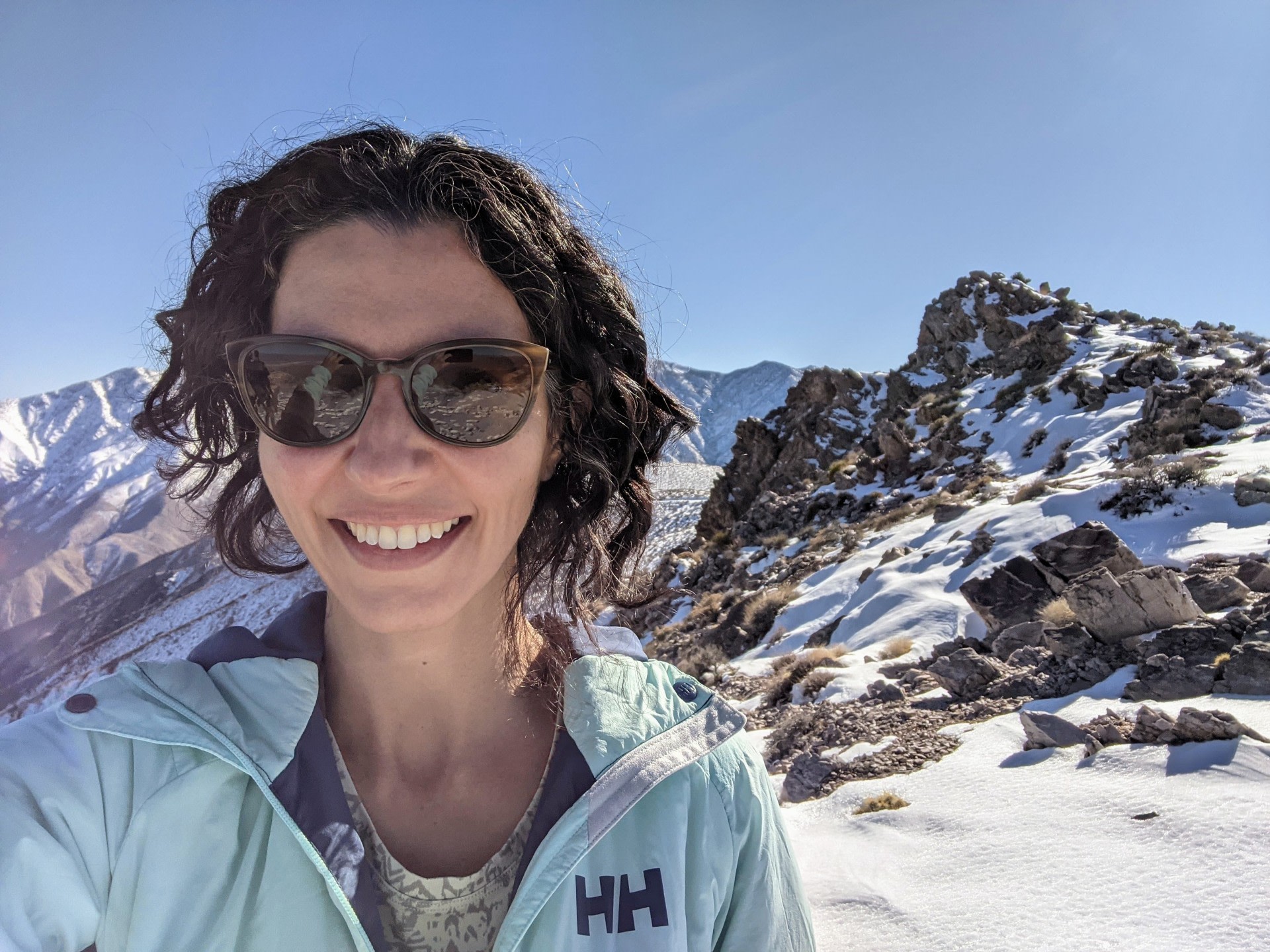 Cassemiro, wearing sunglasses, smiles at the camera, with the snowy, mountainous landscape of Death Valley in the background.
