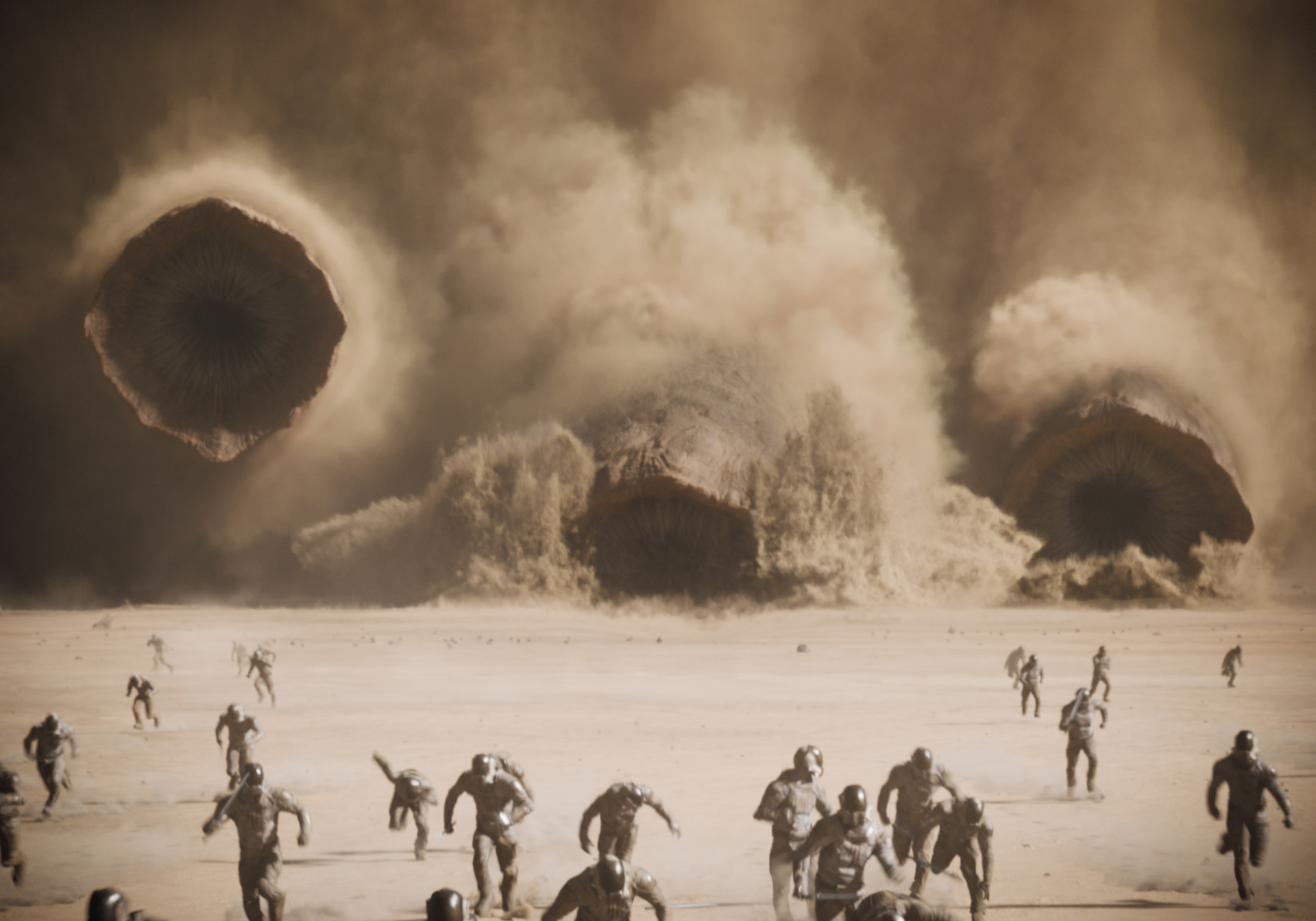 A scene from the film showing people running across the desert as enormous worms erupt from the sand in the background, creating clouds of dust.