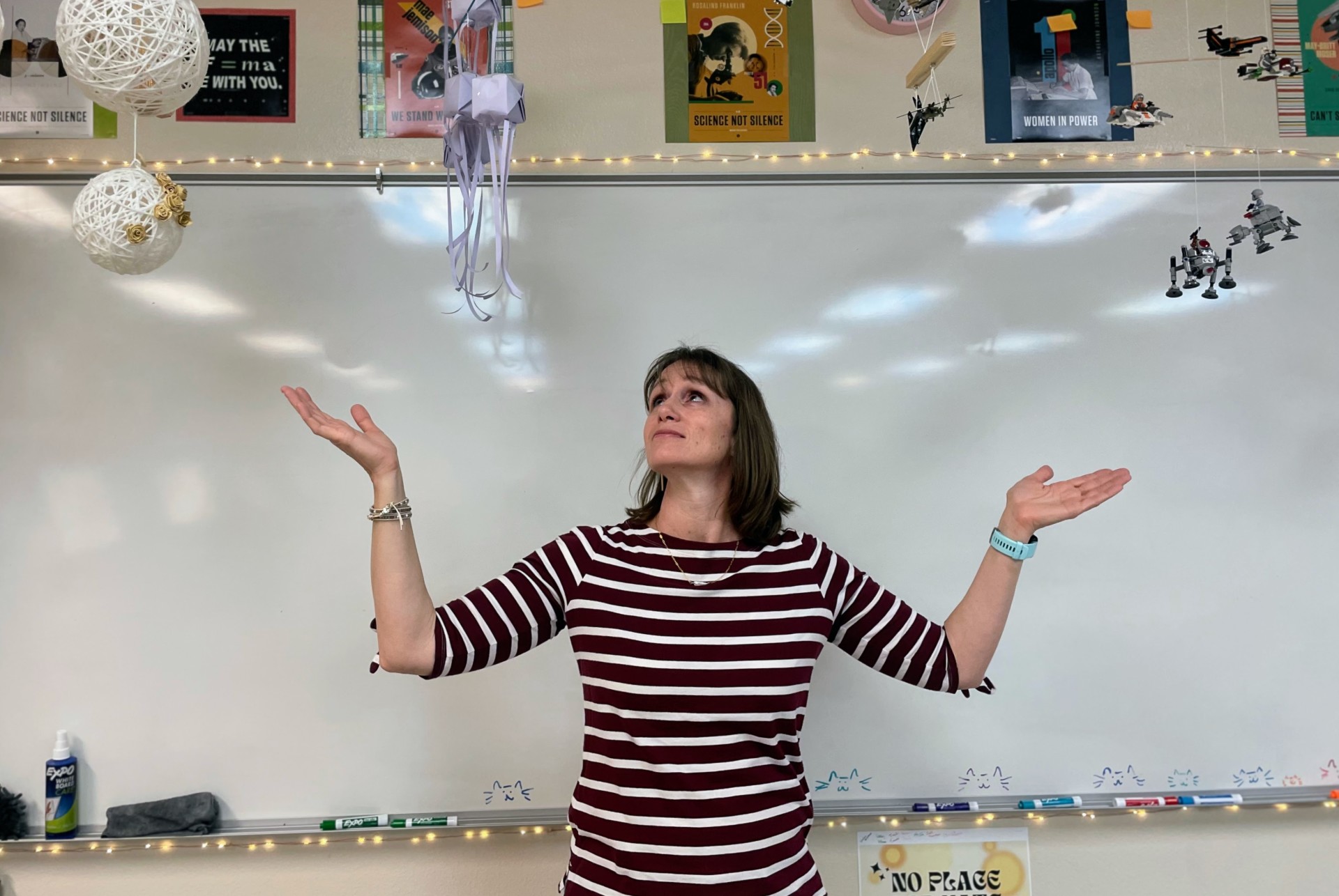 Lynn Jorgensen stands in front of a whiteboard, looking up at an array of colorful hanging mobiles and posters.