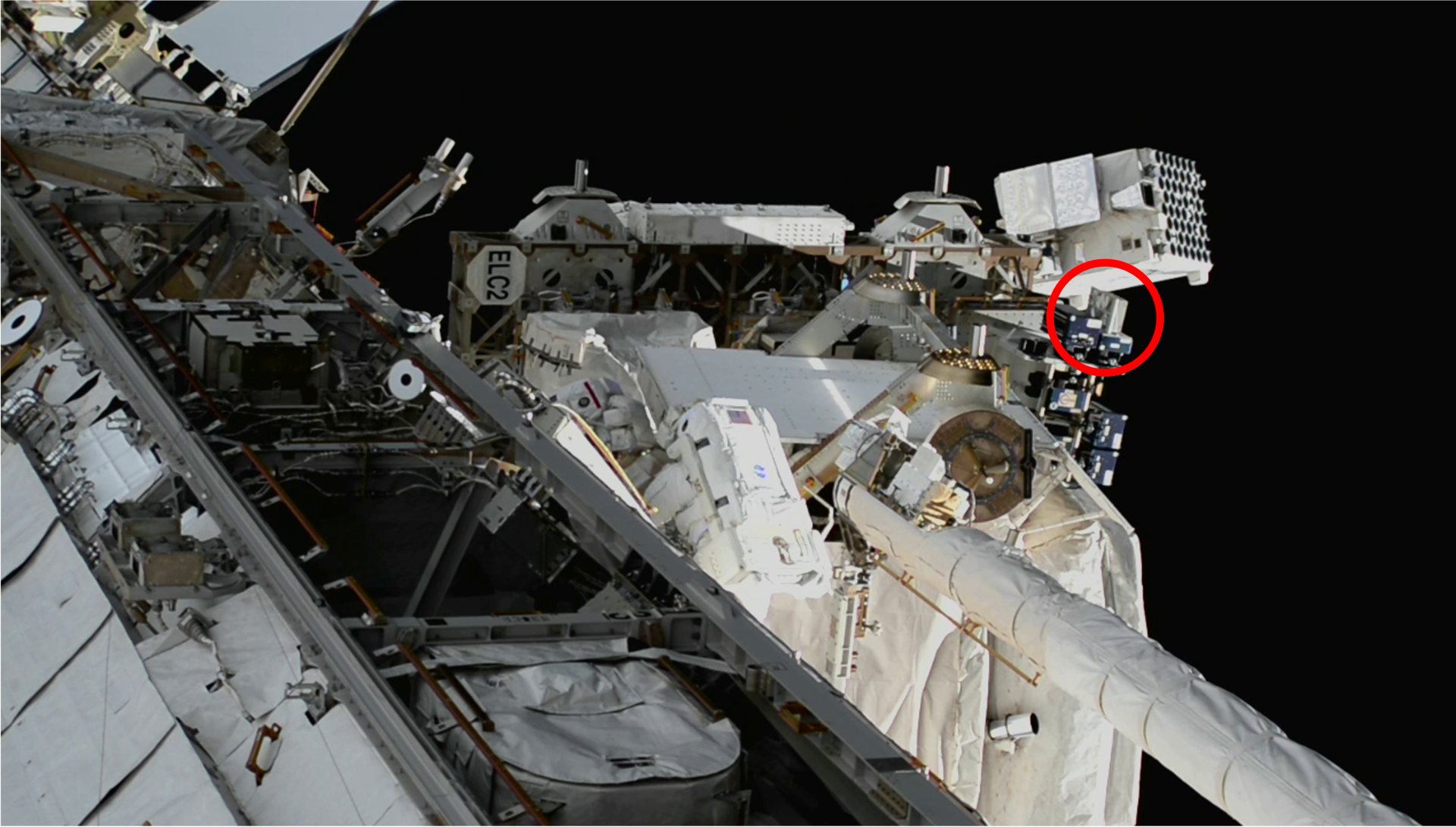Close-up view of the International Space Station exterior, showing equipment and, circled in red, SEAQUE. An astronaut in a spacesuit in the middle of the photo blends into the white station structures.