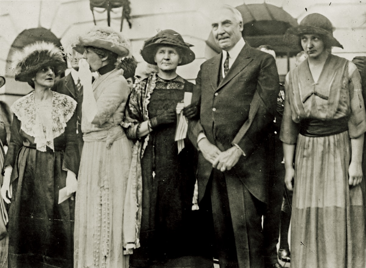 A black-and-white photo of five people, including Marie Curie and President Harding, posing in a row, dressed formally.