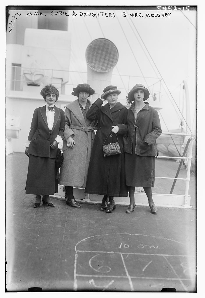 A black-and-white photo of the four women, wearing hats and long overcoats, standing in a row on the deck of a ship.
