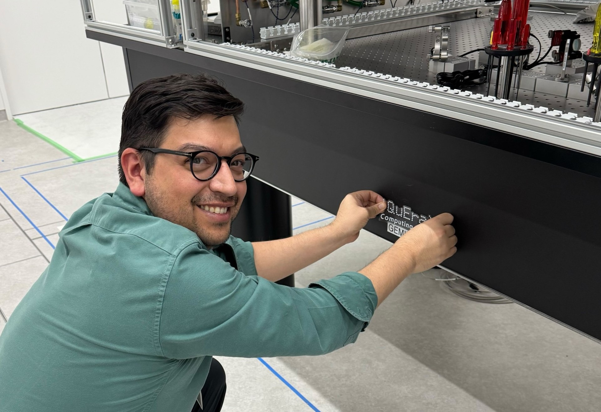 Sergio Cantu looks back over his shoulder while putting a sticker on a piece of quantum equipment.