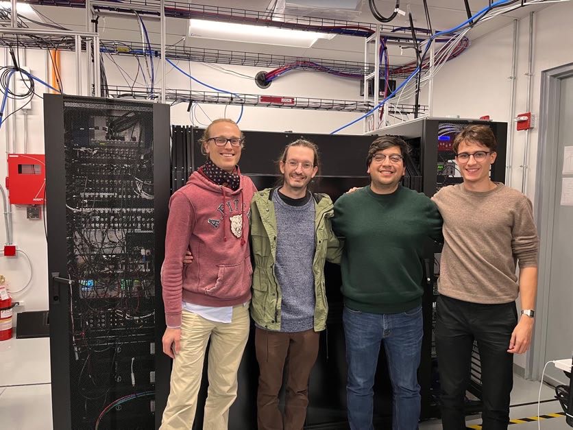 Four members of the science team pose in front of a large quantum computer.